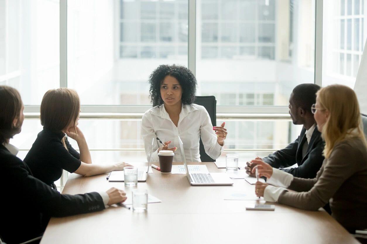 Black female boss leading corporate meeting talking to diverse businesspeople